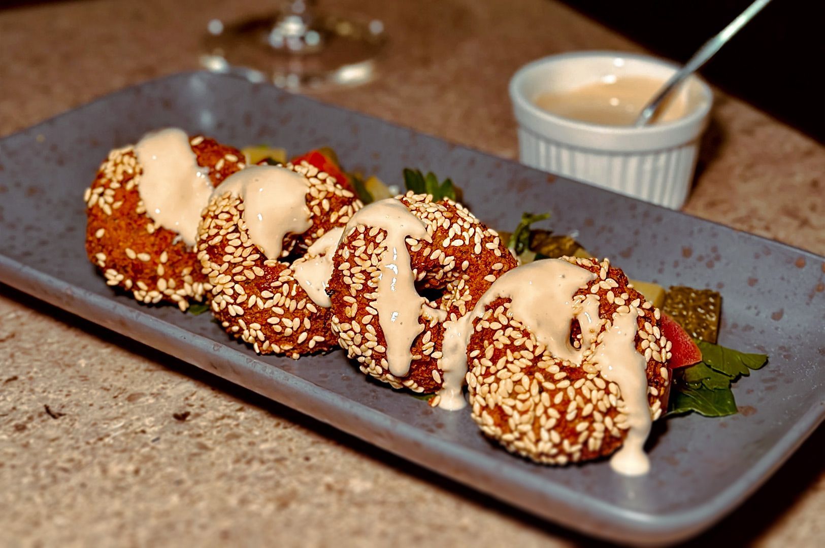 Sesame-crusted stuffed mushrooms drizzled with sauce on a rectangular platter, with dipping sauce nearby