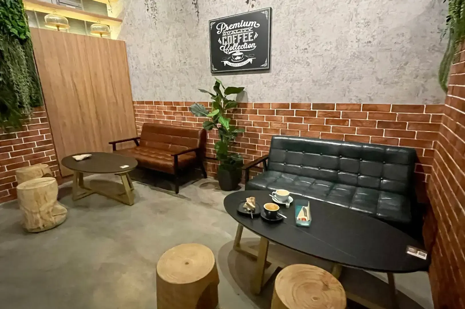 Cozy café lounge with brick walls, black sofa, wooden bench, tables, and stools in a small seating area
