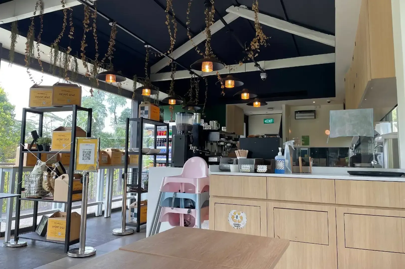 Cozy café interior with hanging lights, display shelves, and a pink chair by the counter.