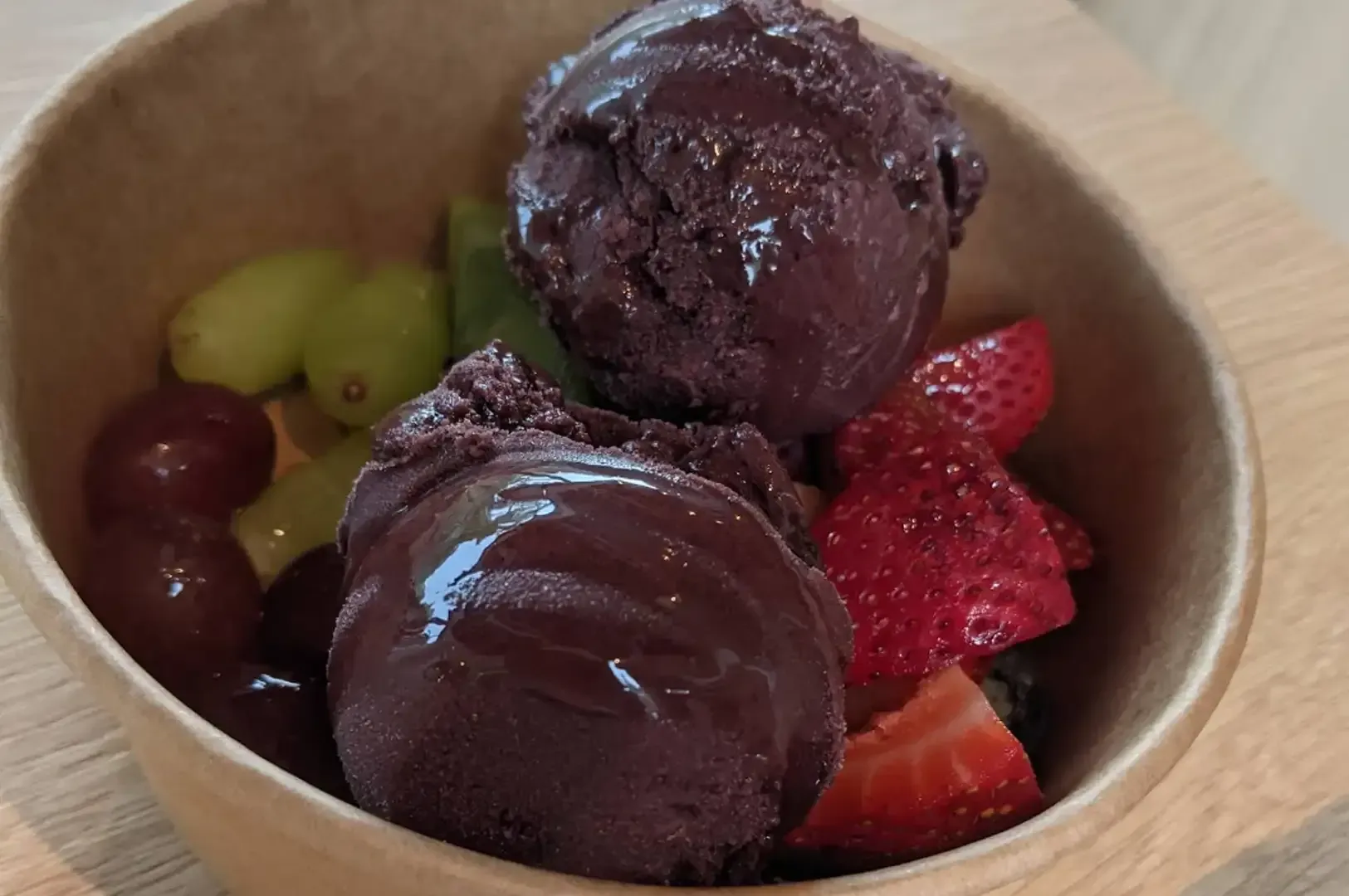 Chocolate-covered ice cream scoops in a wooden bowl with strawberries, grapes, and kiwi slices
