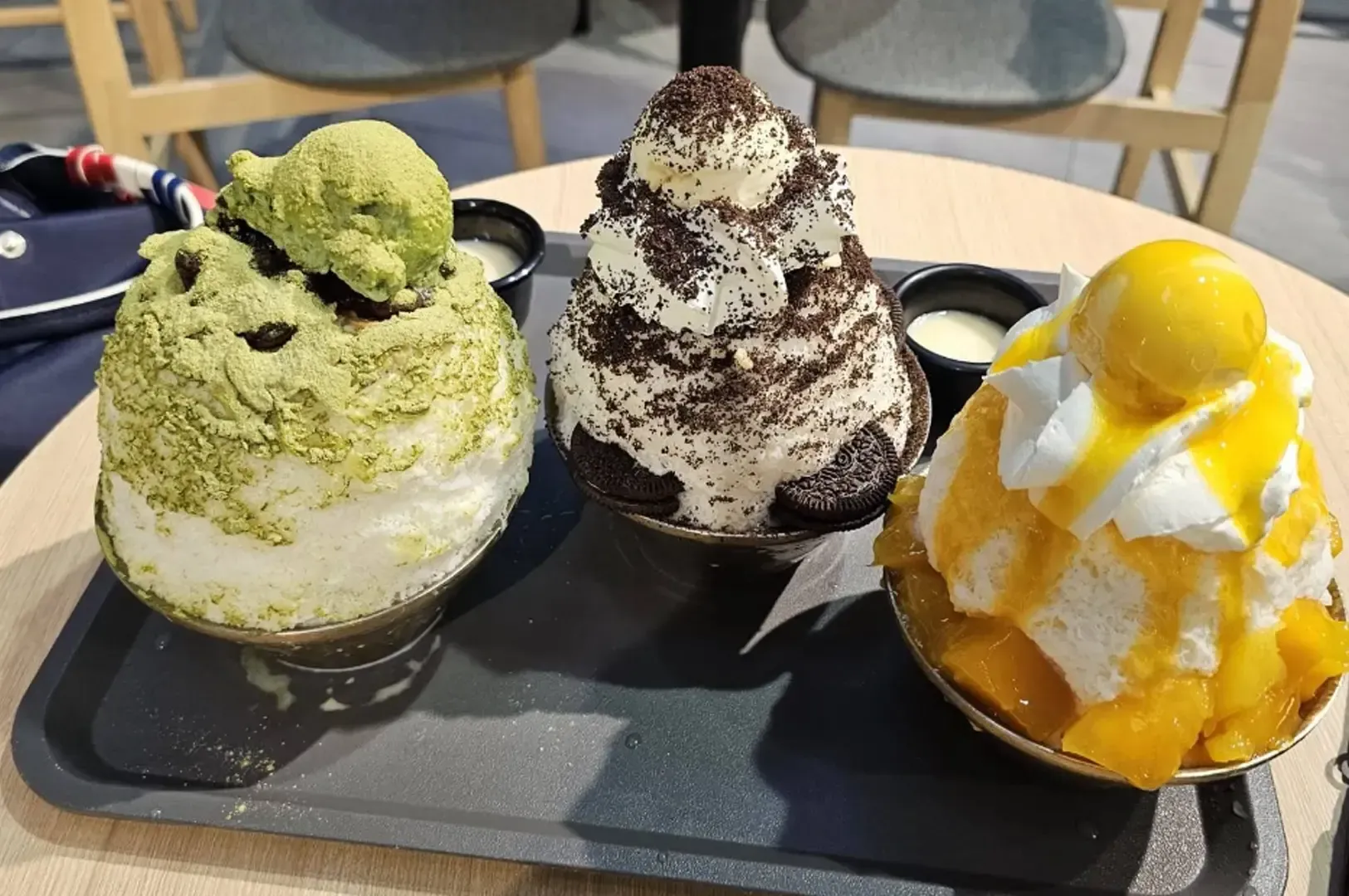 Three colorful shaved ice desserts on a tray at a café table
