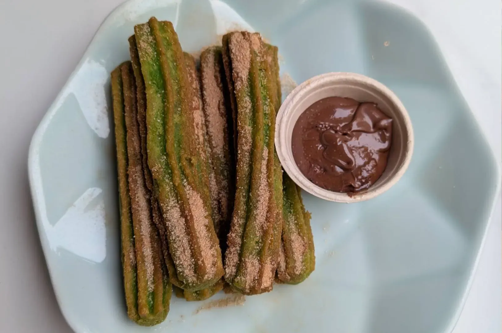 Plate of fried churros dusted with cinnamon, served with a small cup of chocolate dip