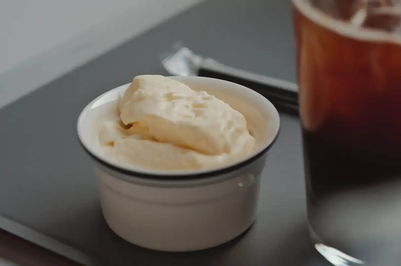 Small white cup of vanilla ice cream beside a glass of iced coffee on a tray