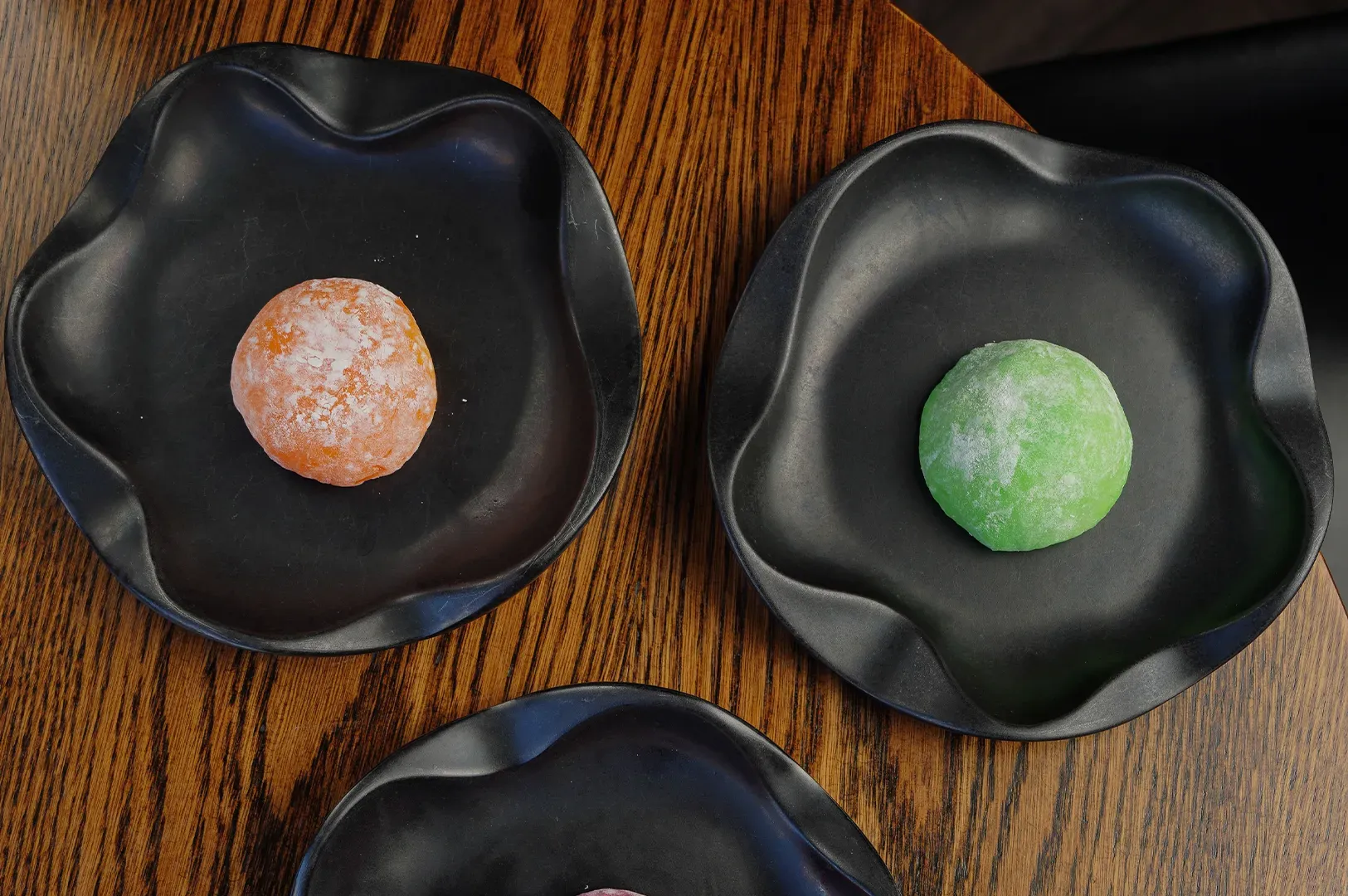 Two black bowls on a wooden table, each holding a round pastel-colored dessert.