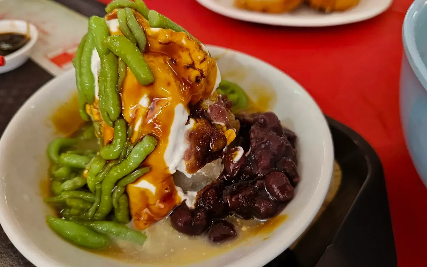 Plate of enchiladas topped with green sauce, beans, and cream on a red tablecloth