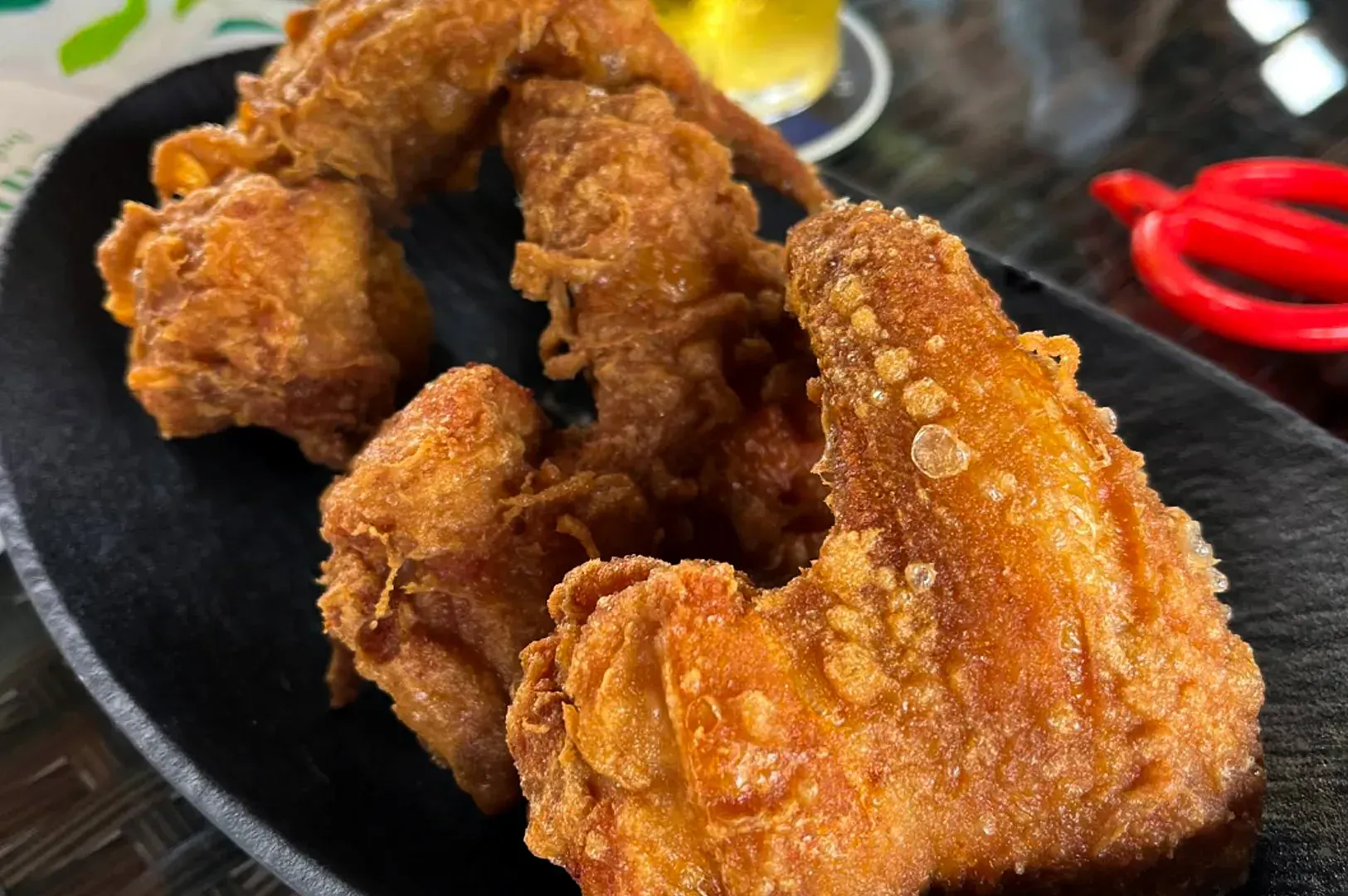Crispy fried chicken wings on a black plate with red chili peppers in the background