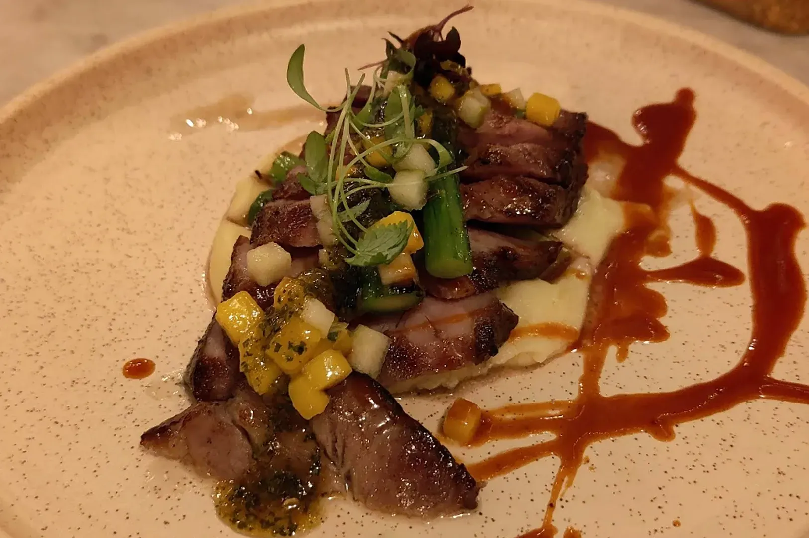 Artfully plated seared meat with garnish and sauce on a beige plate
