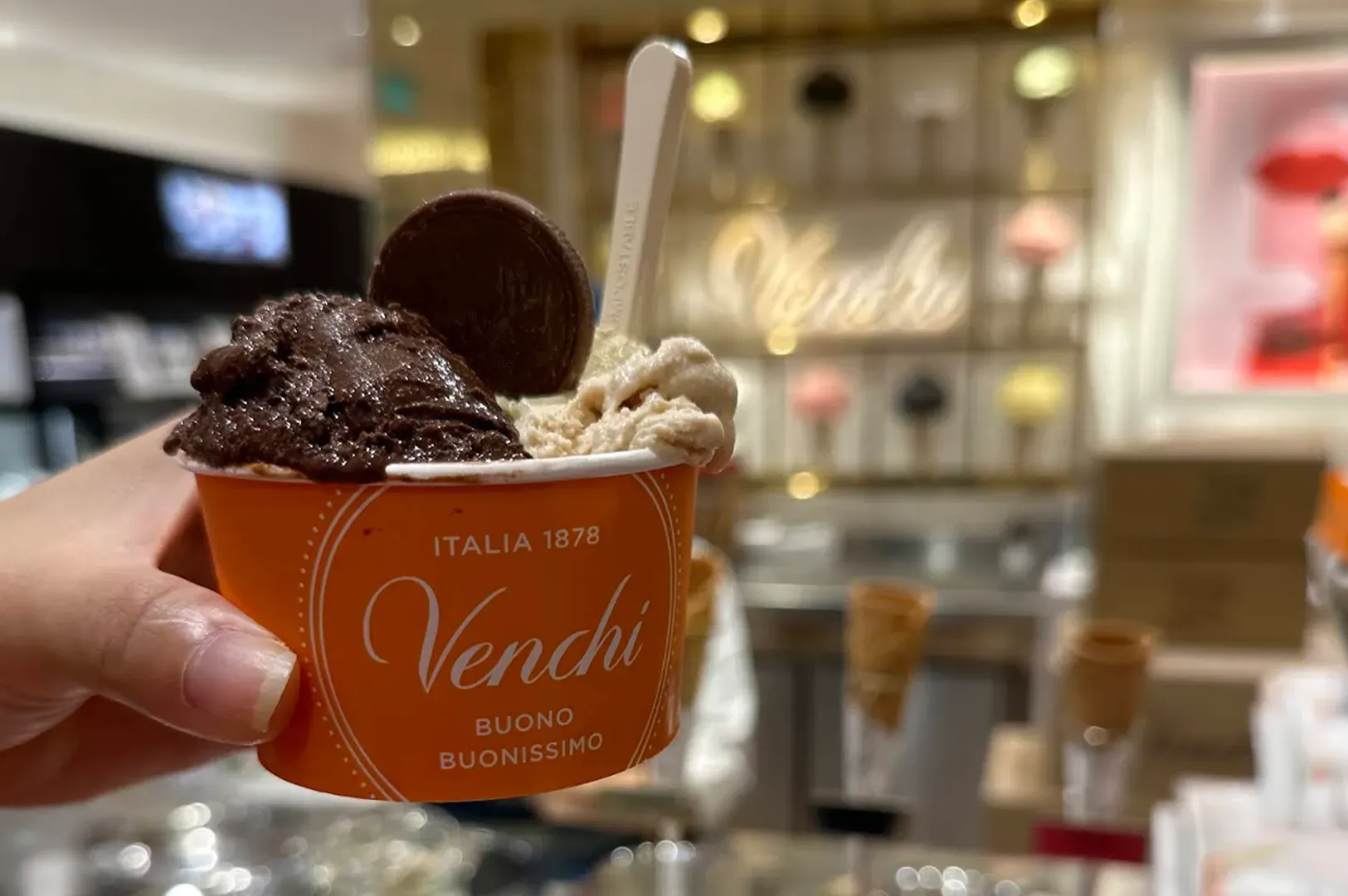 Hand holding a cup of Venchi gelato with chocolate and cream in a bright shop