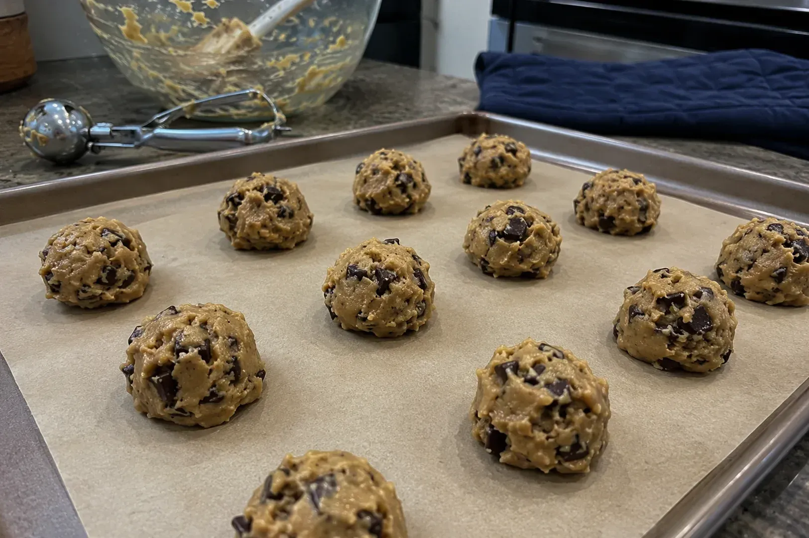 Scoops of cookie dough on a parchment-lined baking sheet in a kitchen.