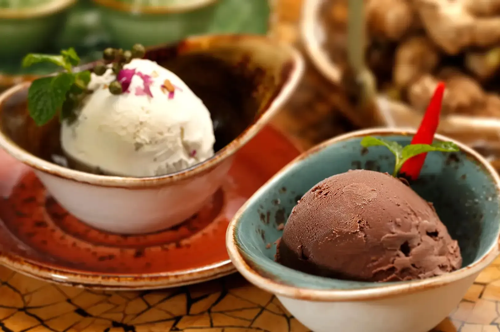Two bowls of ice cream with mint and cherries on a patterned table