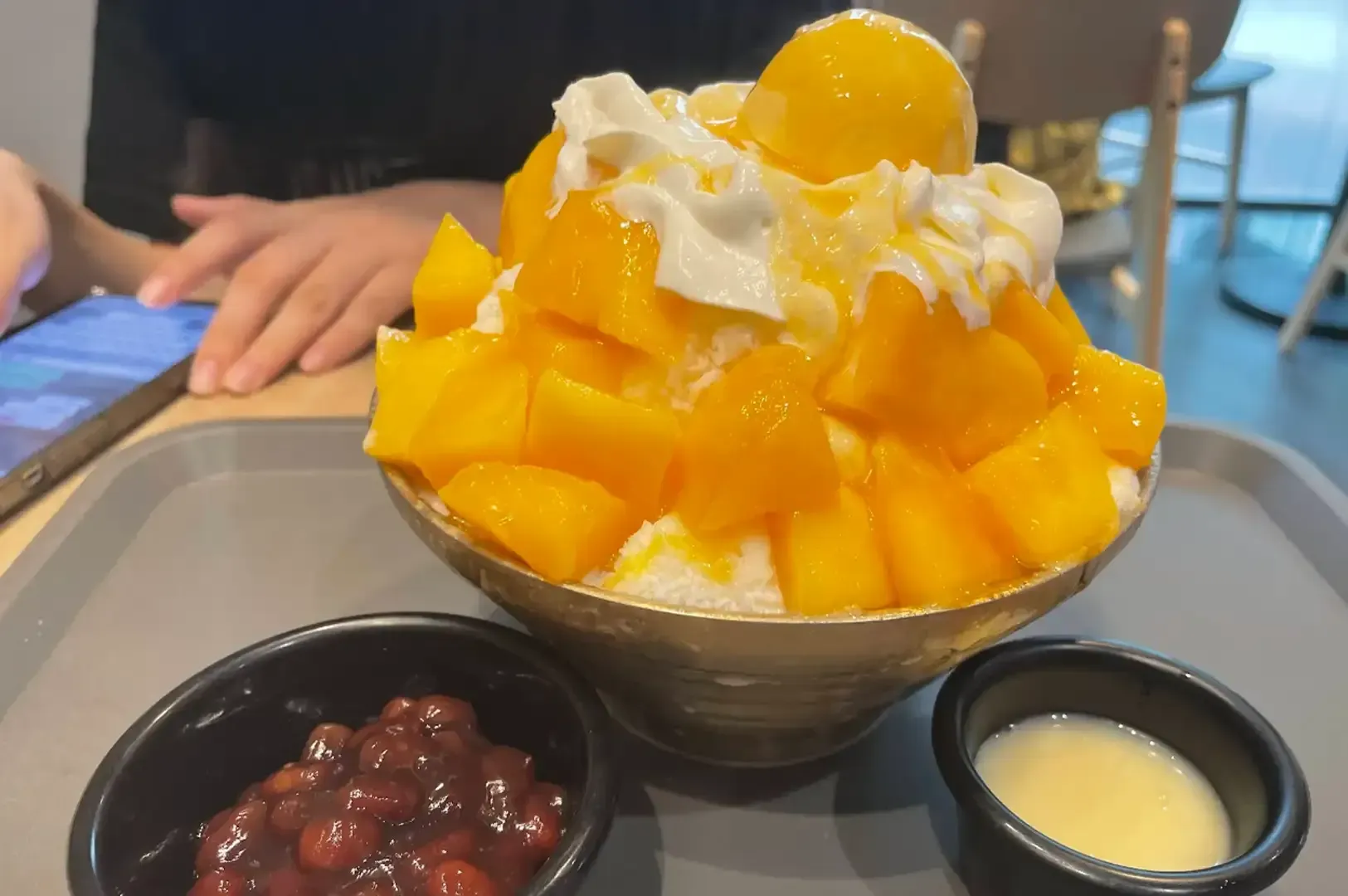 Mango shaved ice dessert topped with whipped cream, with red beans and condensed milk on the side