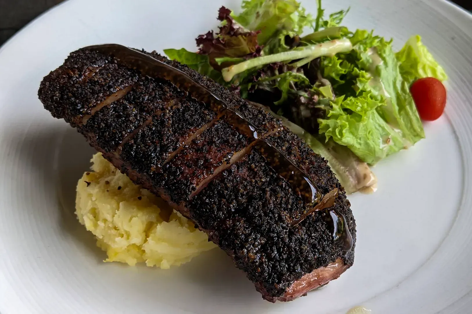 Grilled steak with mashed potatoes and green salad on a white plate