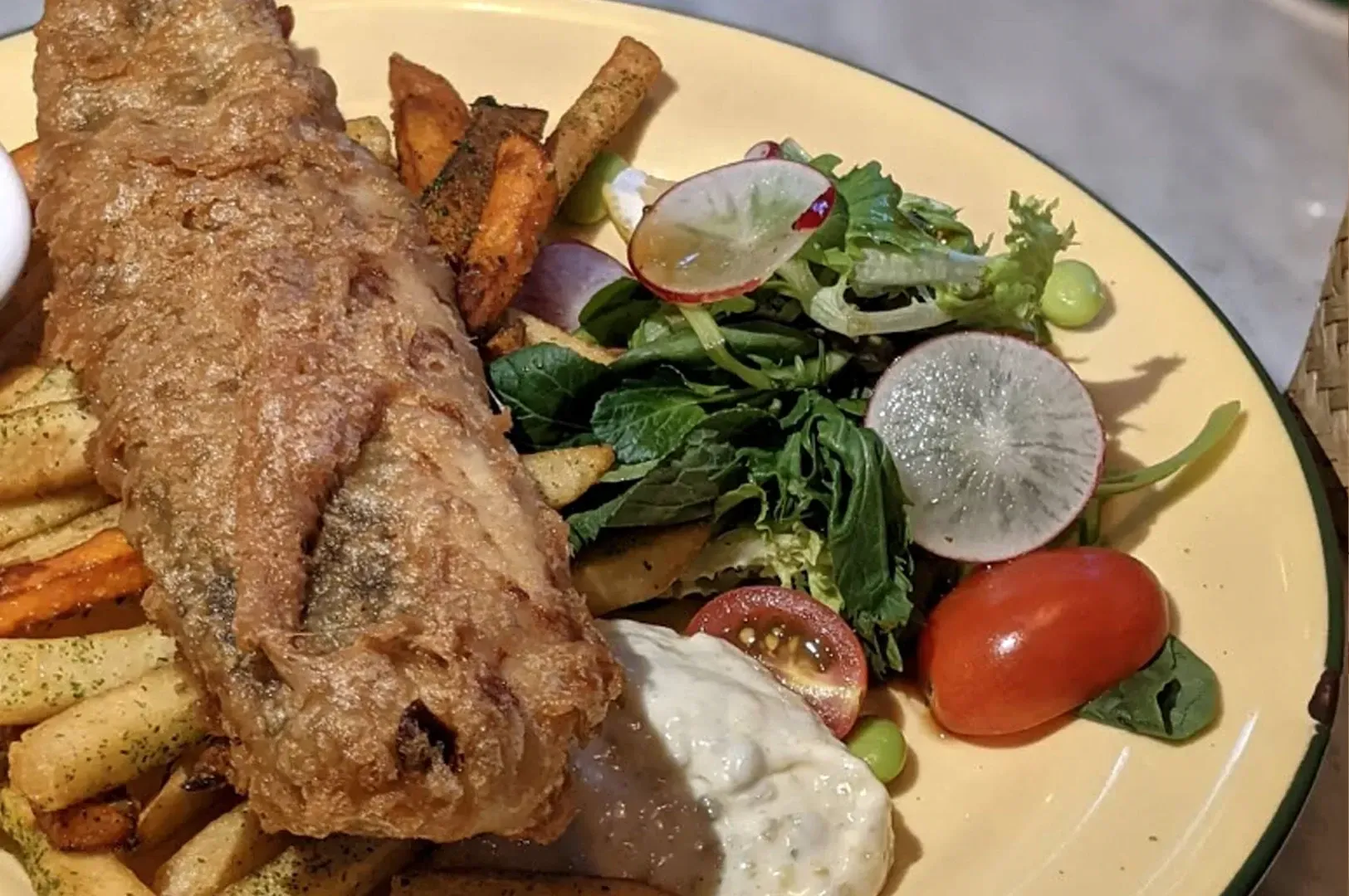 Fried fish with fries, salad, and dipping sauce on a yellow plate