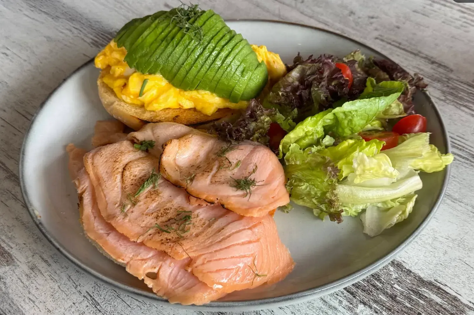 Plated salmon with avocado fan and mixed green salads on a white plate