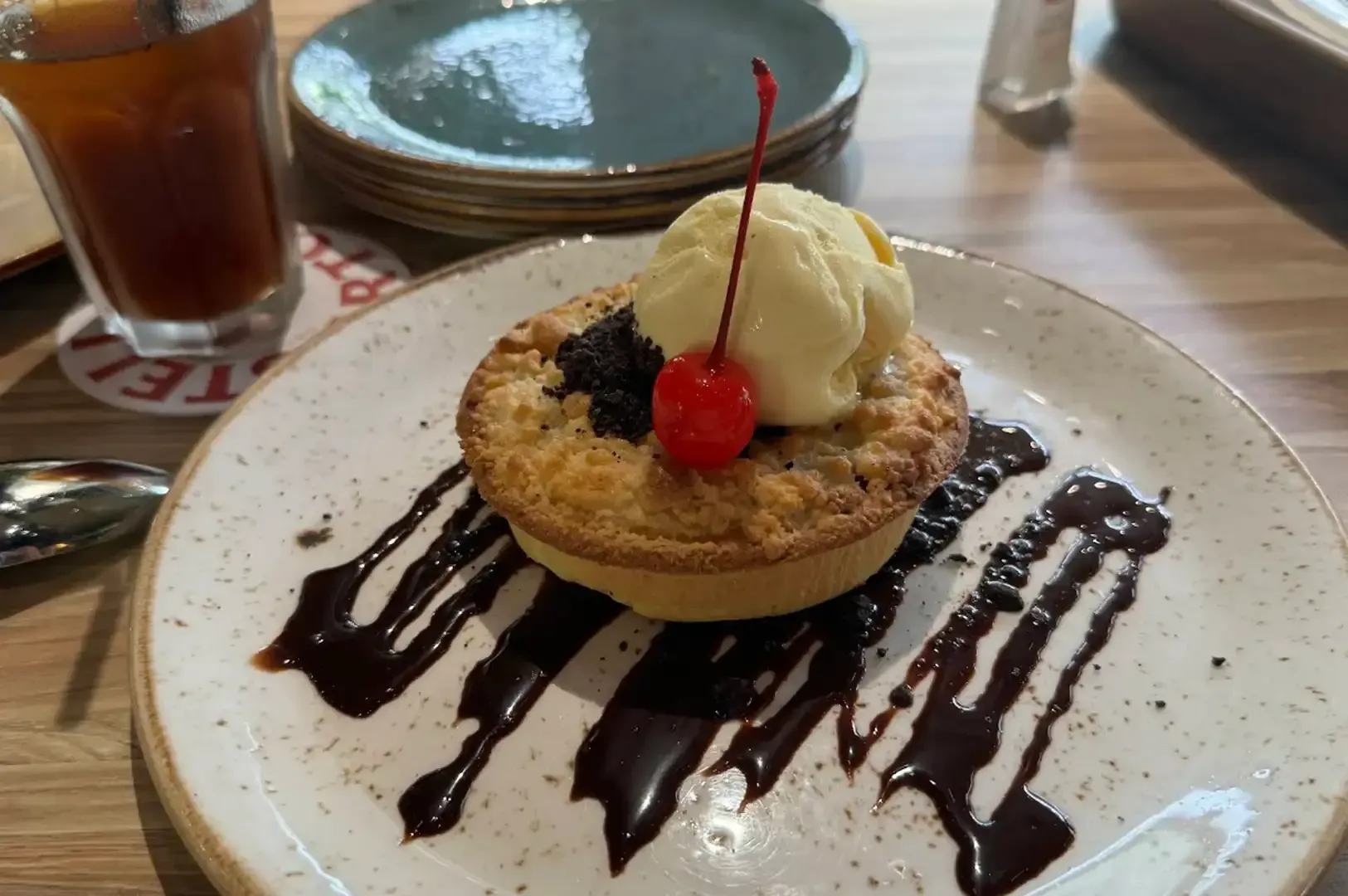 Dessert tart with vanilla ice cream and cherry, drizzled chocolate on a plate at a café table