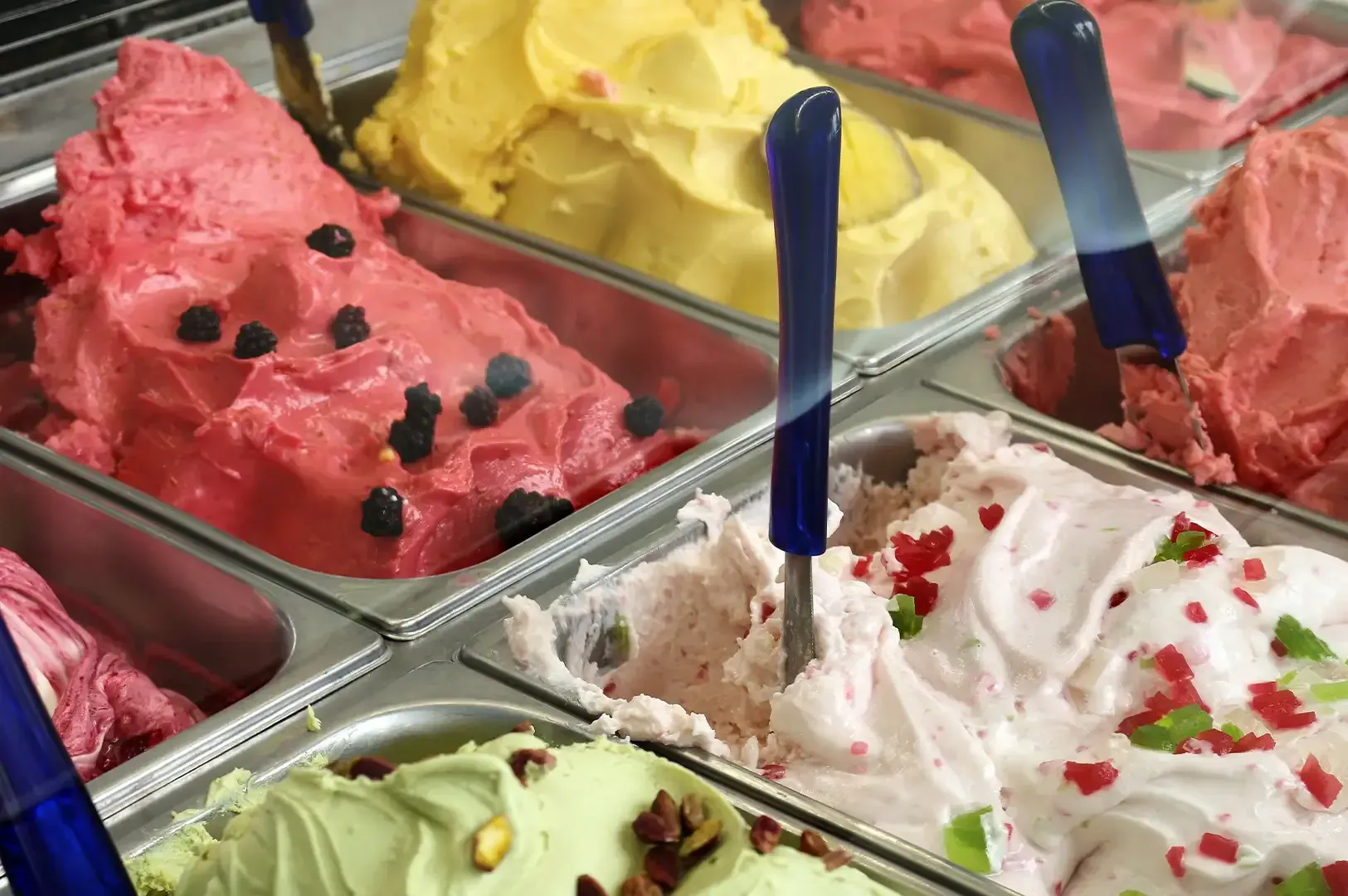 Trays of colorful gelato with blue serving spoons in a display case