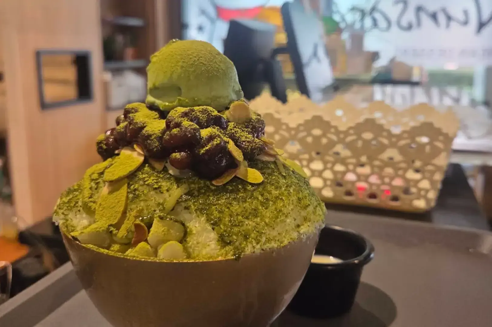 Green shaved ice dessert topped with red beans in a café bowl