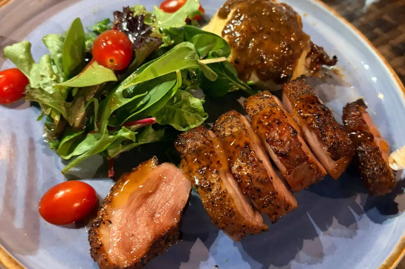 Grilled sliced meat with salad and cherry tomatoes on a blue plate