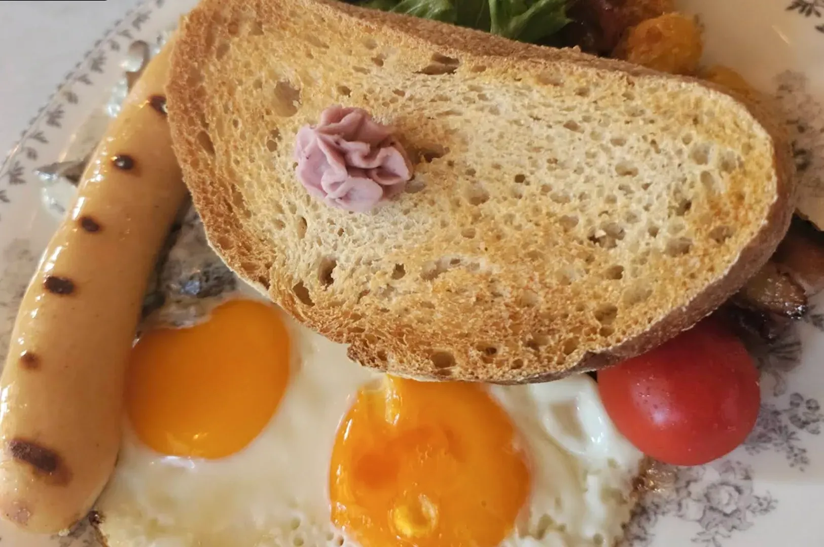 Breakfast plate with toast, sausage, eggs, tomato, and a small purple garnish