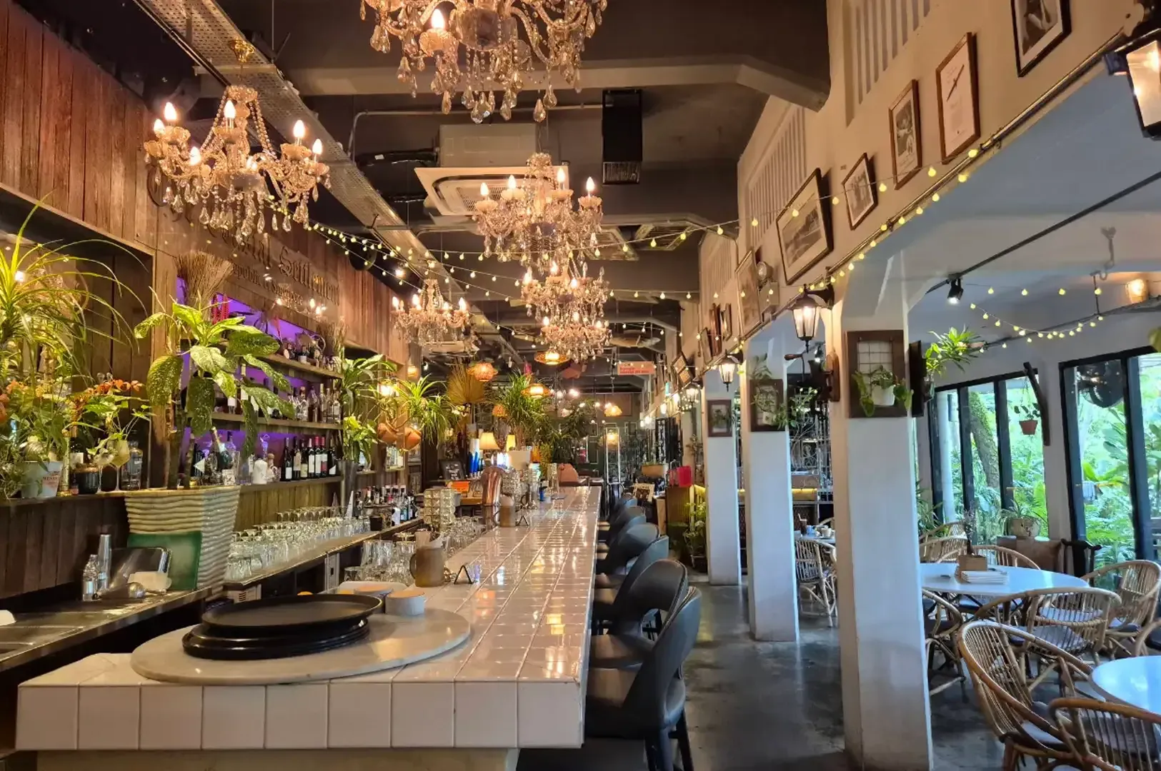Elegant restaurant interior with chandeliers, a marble bar, plants, and window seating area