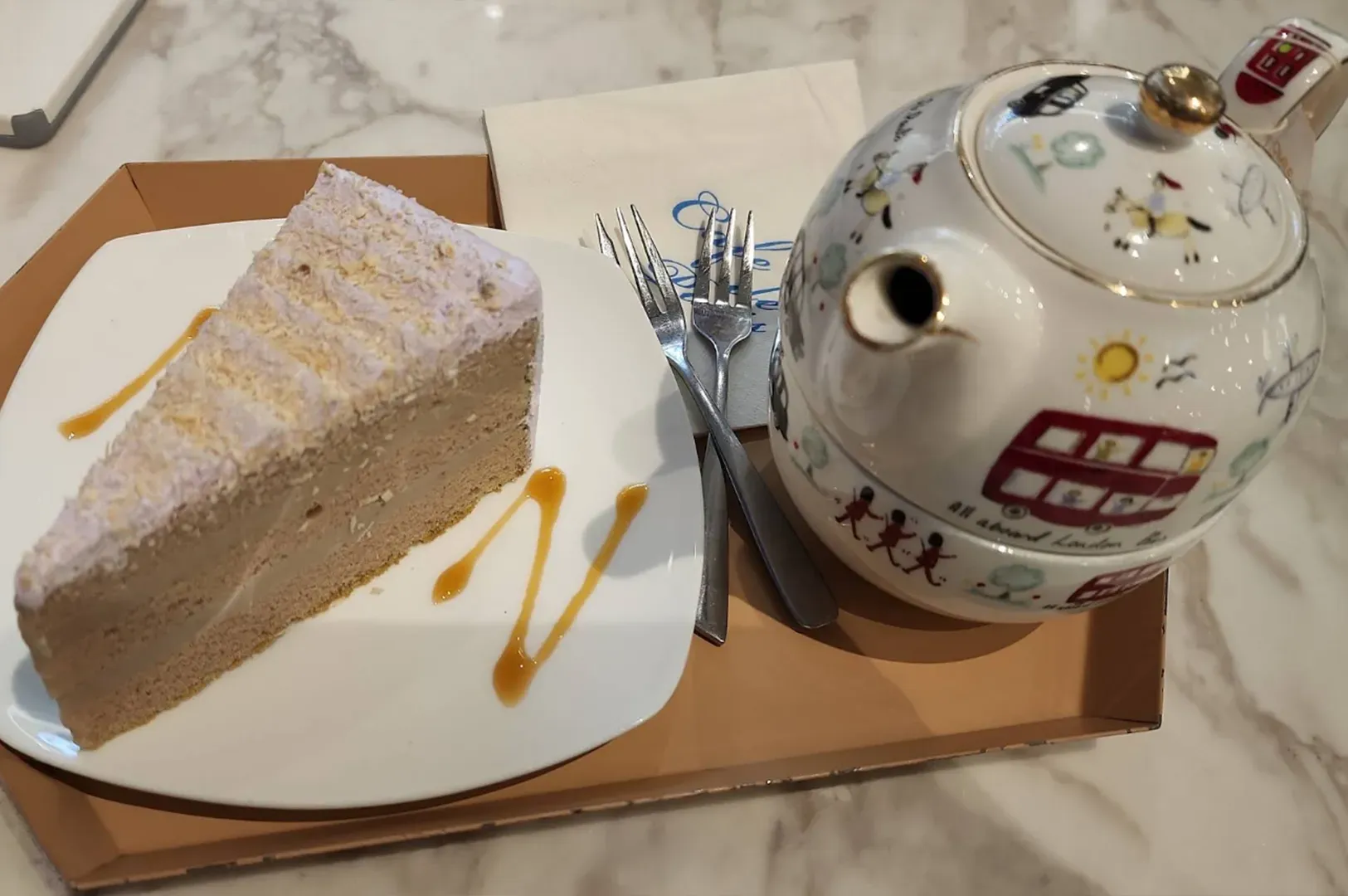 Slice of cake and a ceramic teapot on a tray table in a cafe-like setting