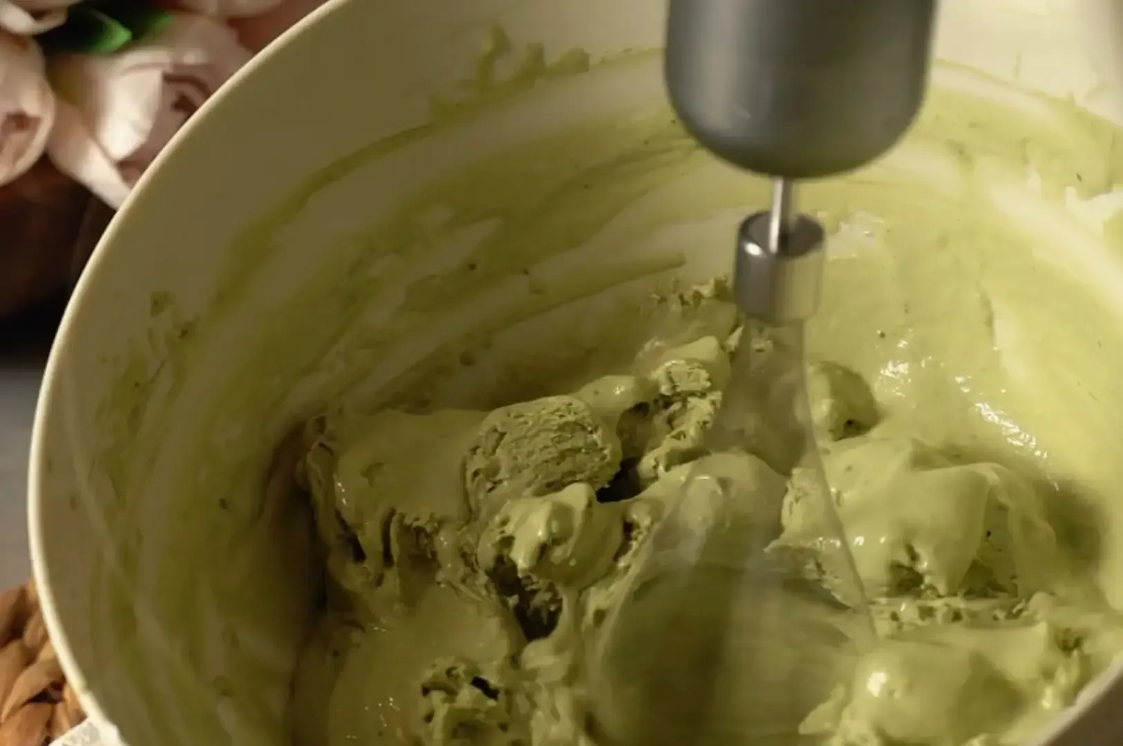 A hand mixer blending green batter in a bowl