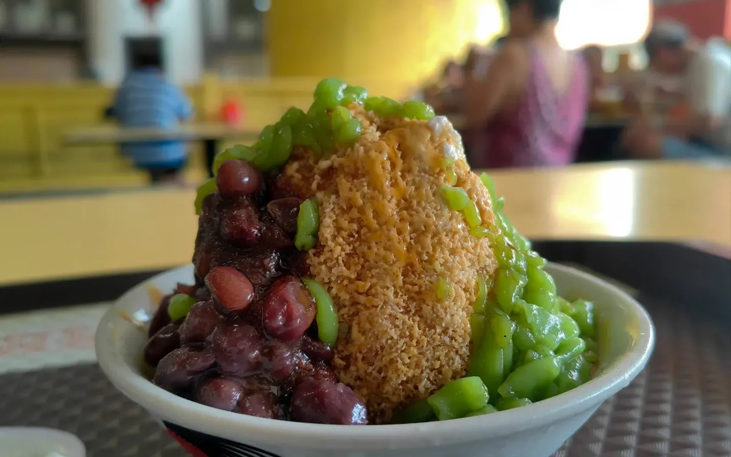 Dessert bowl topped with green sauce and red beans, with a golden fried cake in the center