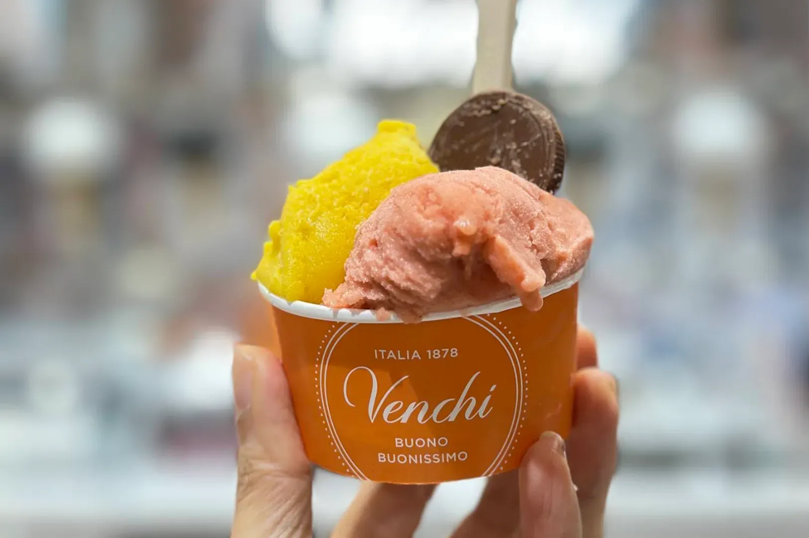Hand holding a Venchi gelato cup with yellow, pink, and chocolate scoops