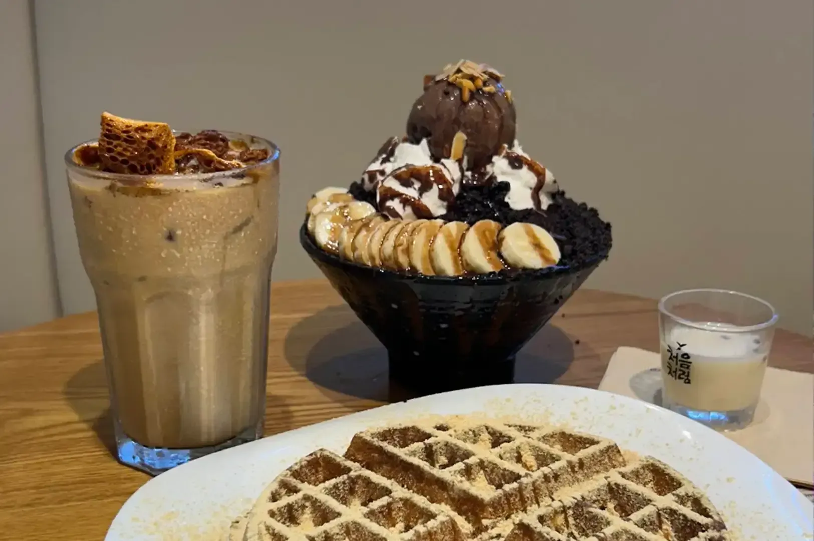 Dessert table with waffles, a milkshake, a banana-topped sundae, and a small drink