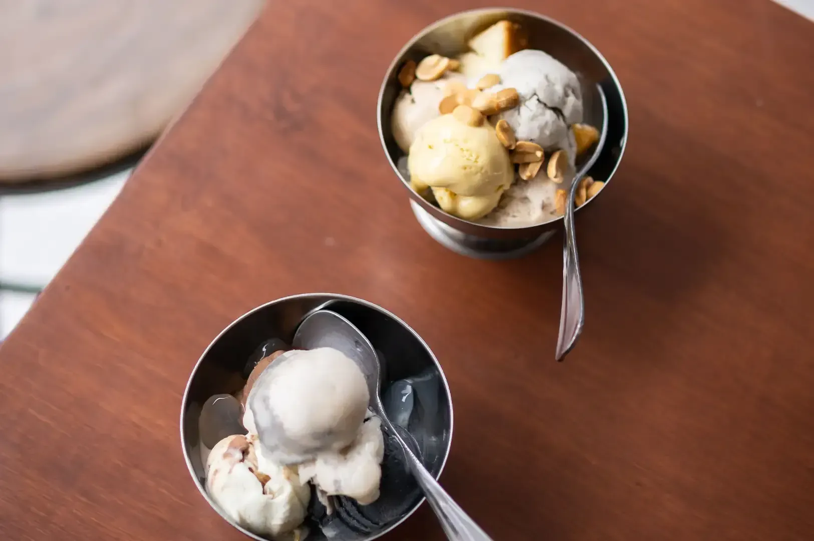 Two bowls of ice cream on a wooden table, each with a spoon