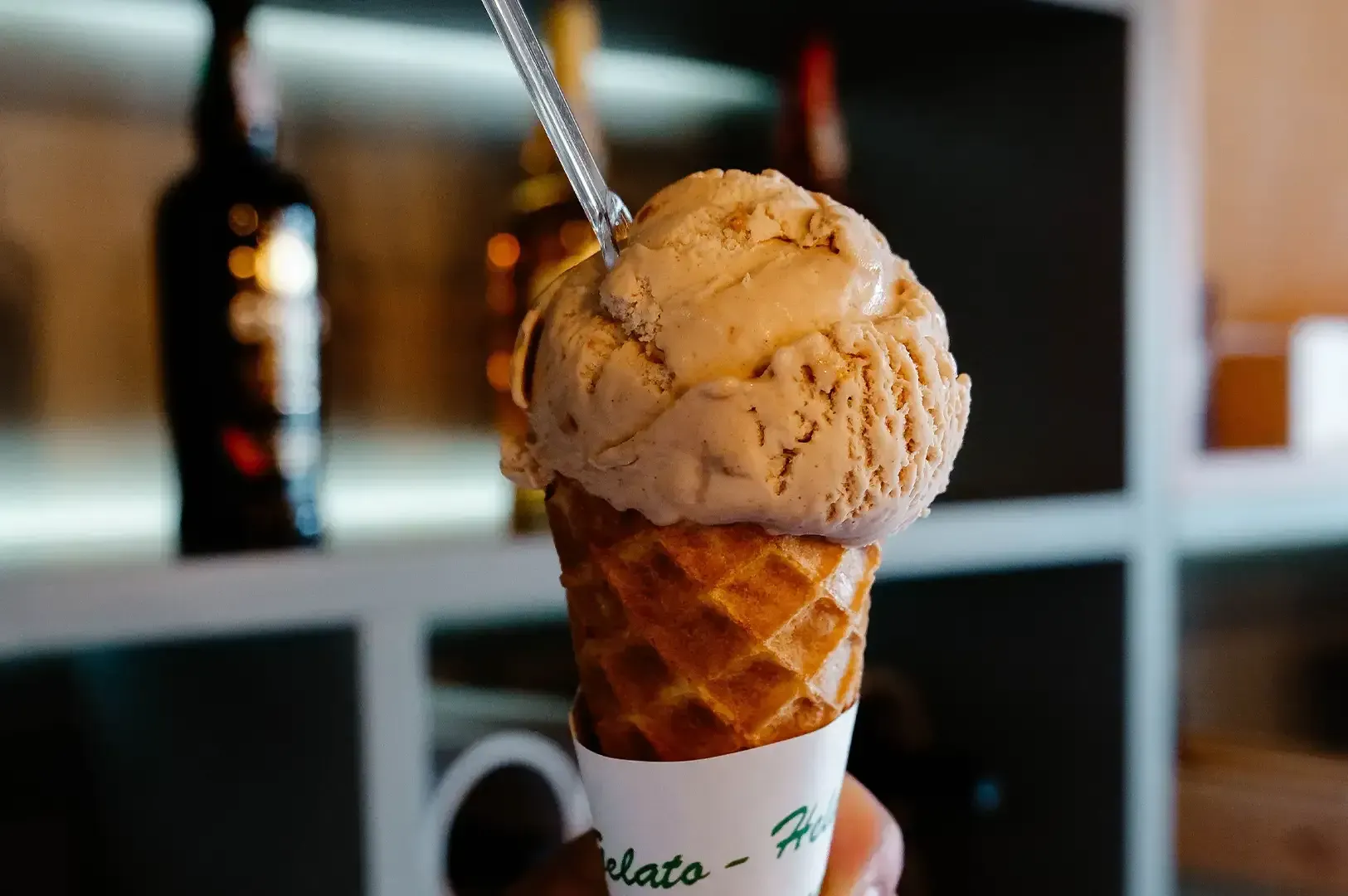Scoop of caramel ice cream in a waffle cone with a spoon in a café setting