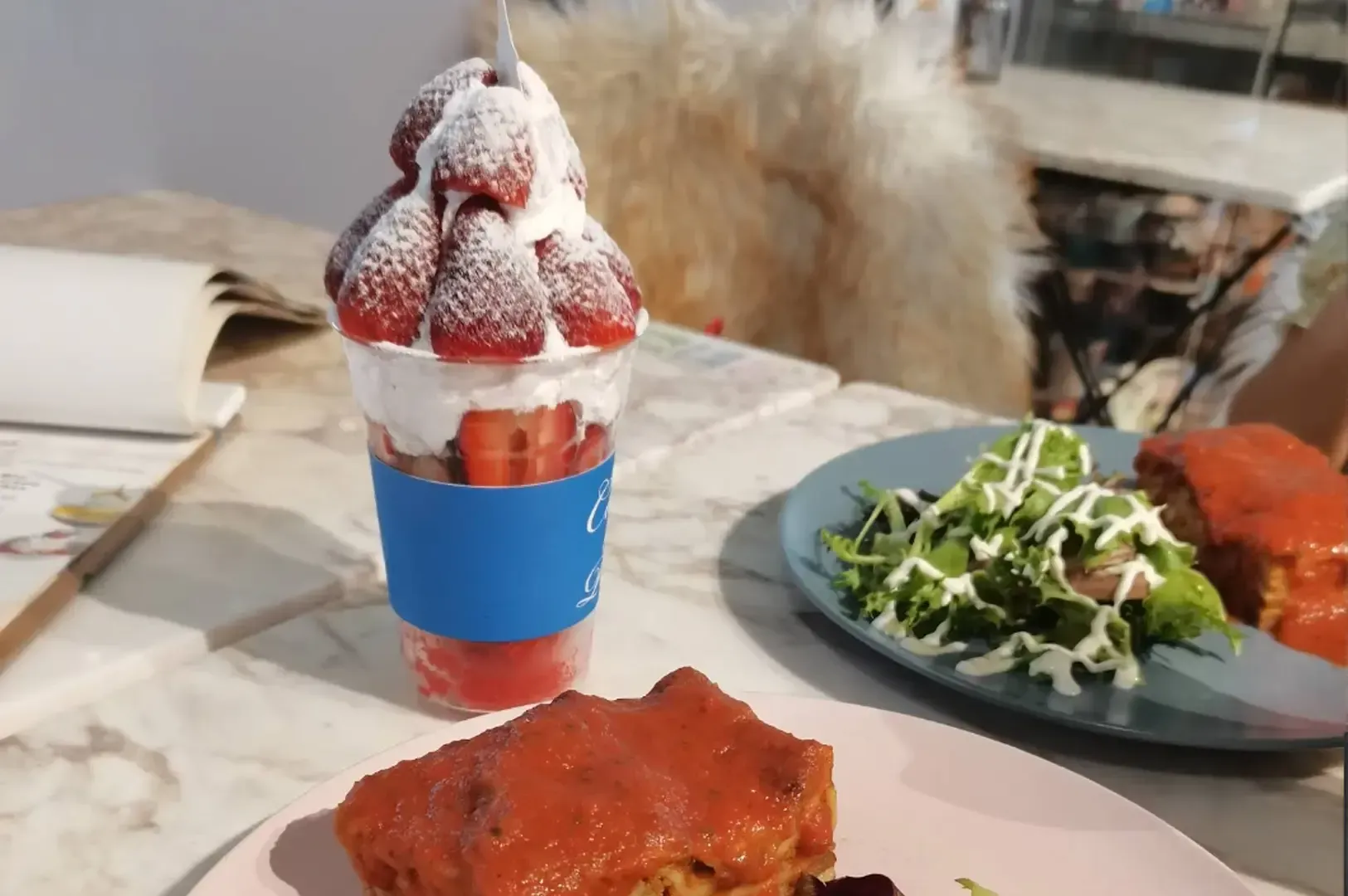 Table setting with a strawberry dessert drink, salad, and a plated meal on a marble surface