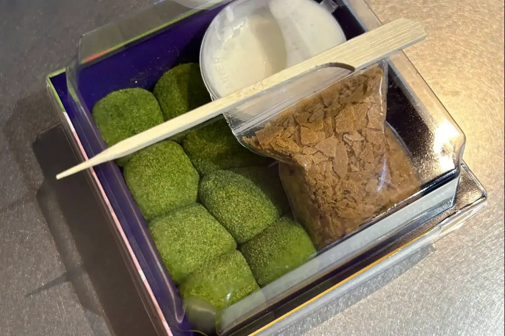 Assorted Japanese sweets in a tray, with green mochi, white dumplings, and a brown dessert topped with a wooden pick