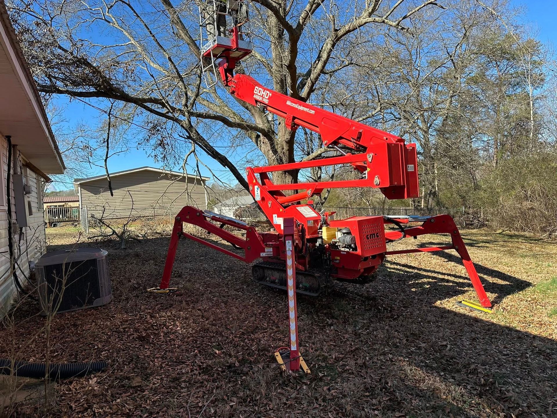 Red spider lift operating near a house and tree on a sunny day.