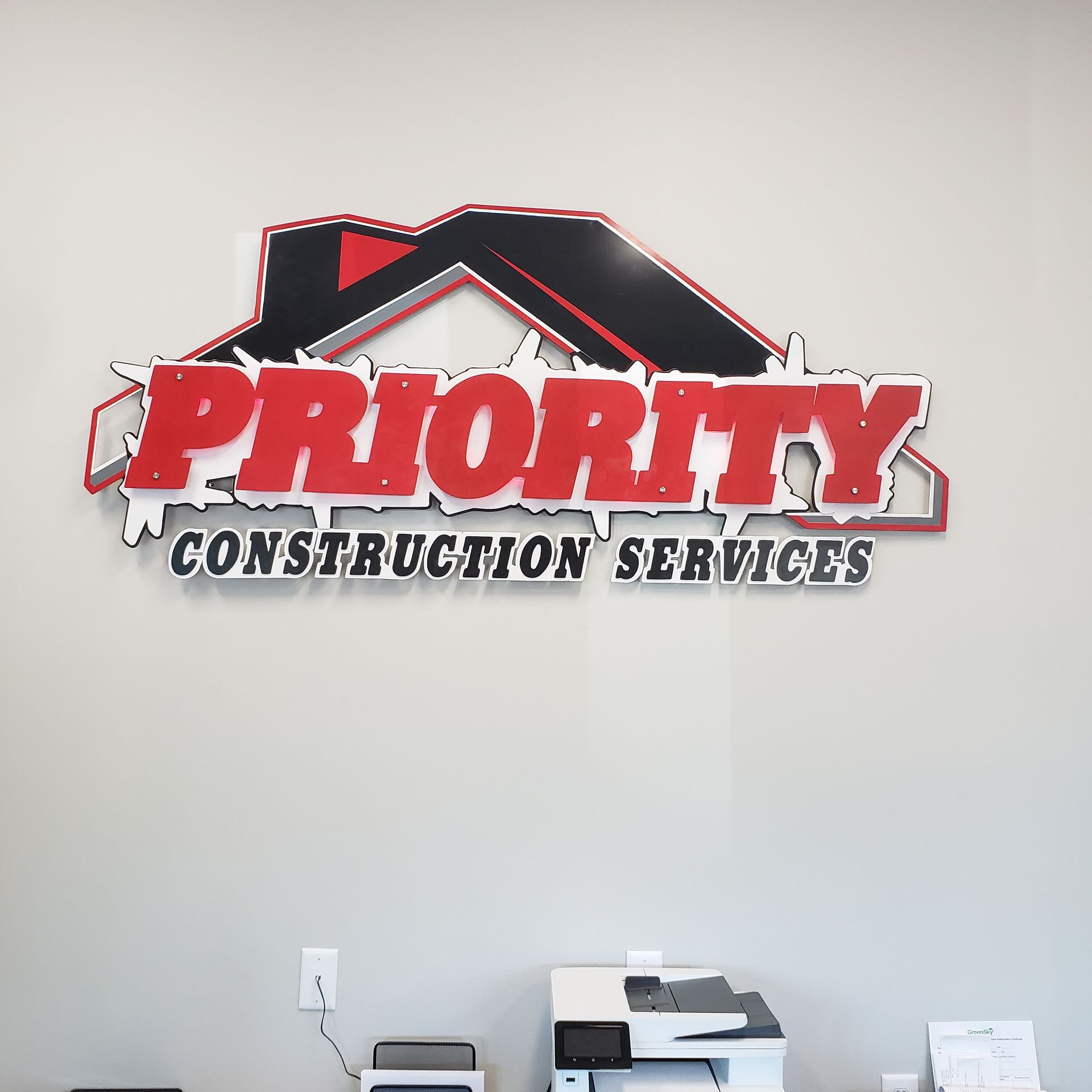 Logo for Priority Construction Services on a wall. Red, black, and white colors.