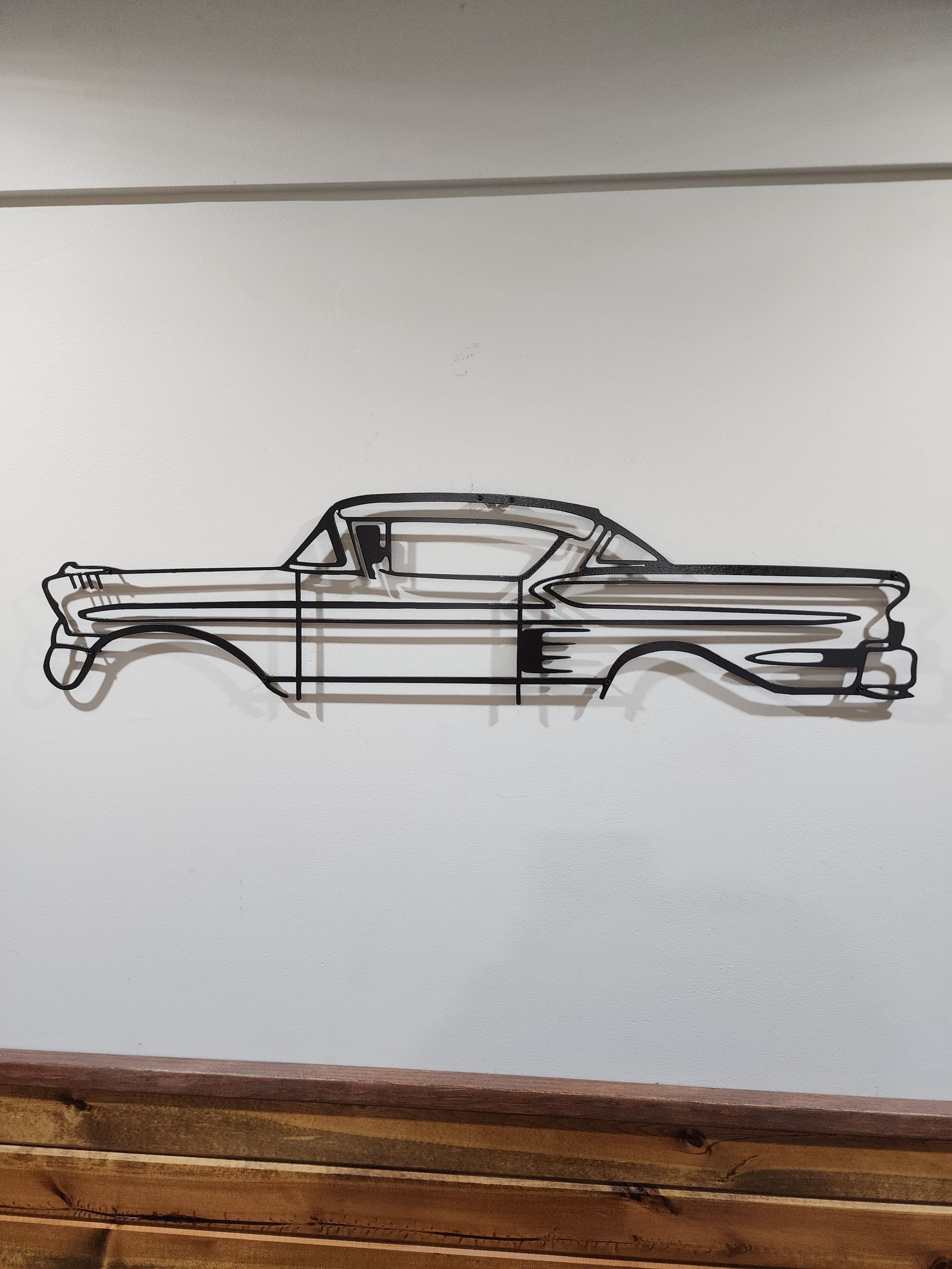 Metal sculpture of a classic car, mounted on a white wall.