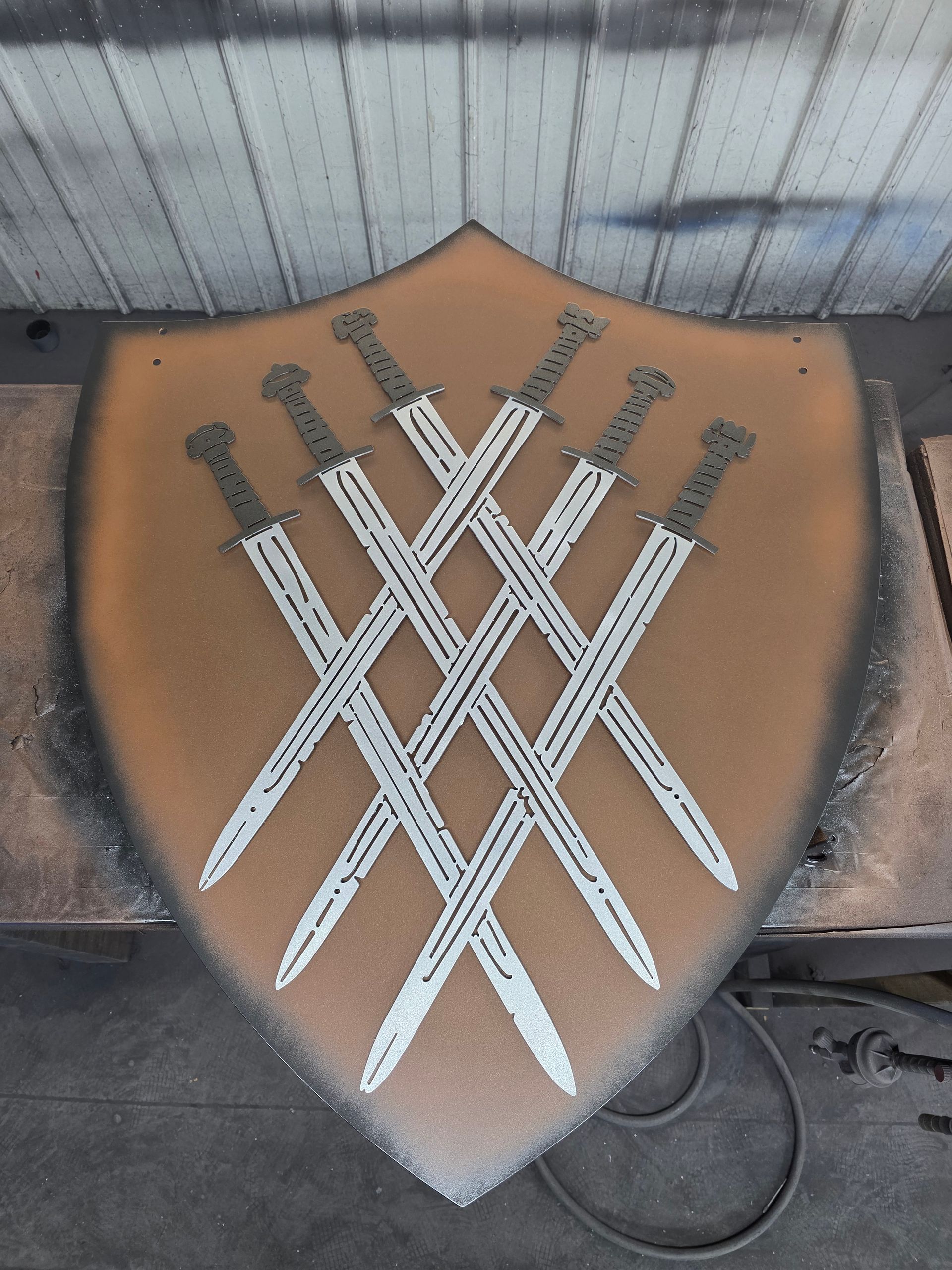 Shield with six crossed swords on a brown background, with a black border.