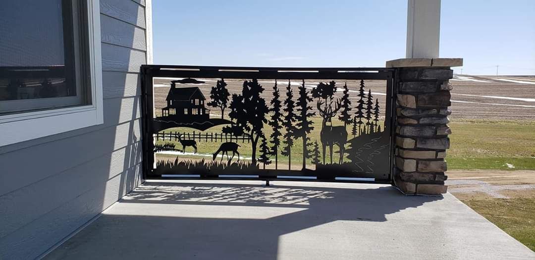 A decorative metal fence with a landscape design on a porch, next to a stone-covered column.