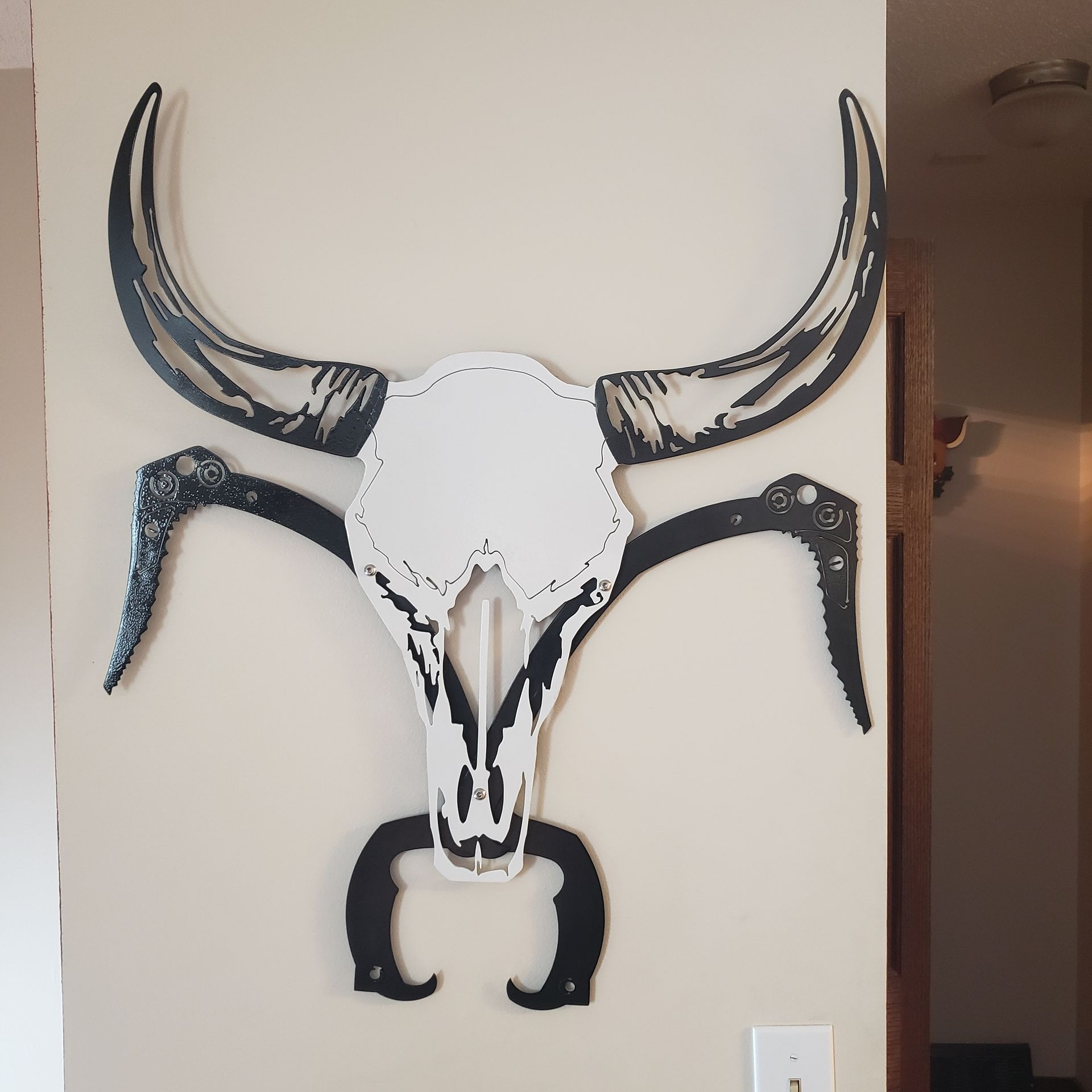 Metal bull skull wall art, black horns and accents on a white skull.