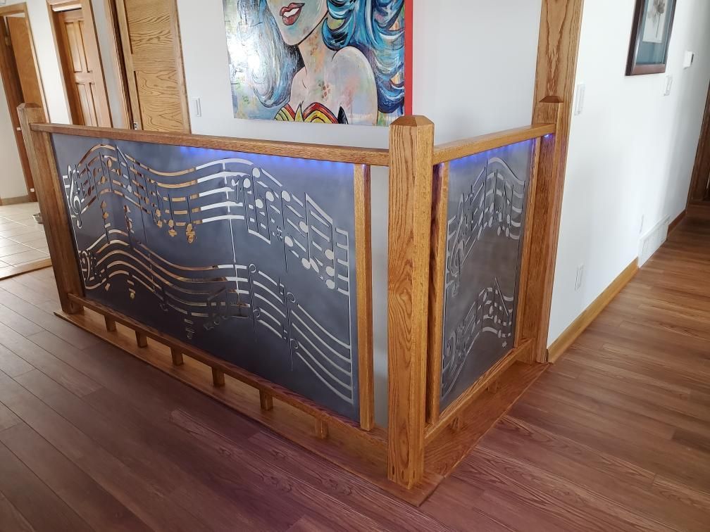 Wooden railing with cut metal panels featuring musical notes, lit by blue lights, in a home.