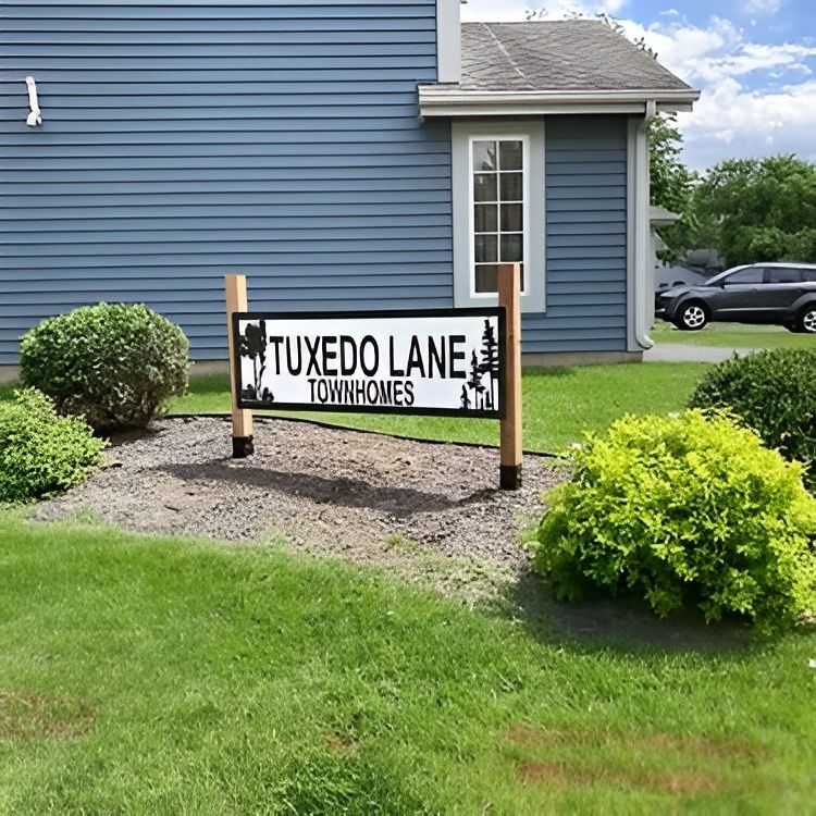 Sign for Tuxedo Lane Townhomes in front of a blue building, on a grassy area with bushes.