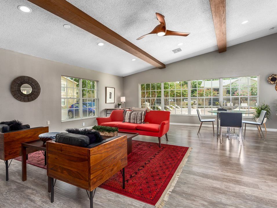 Living room with red sofa, rug, and modern wood chairs. Large windows, beams.
