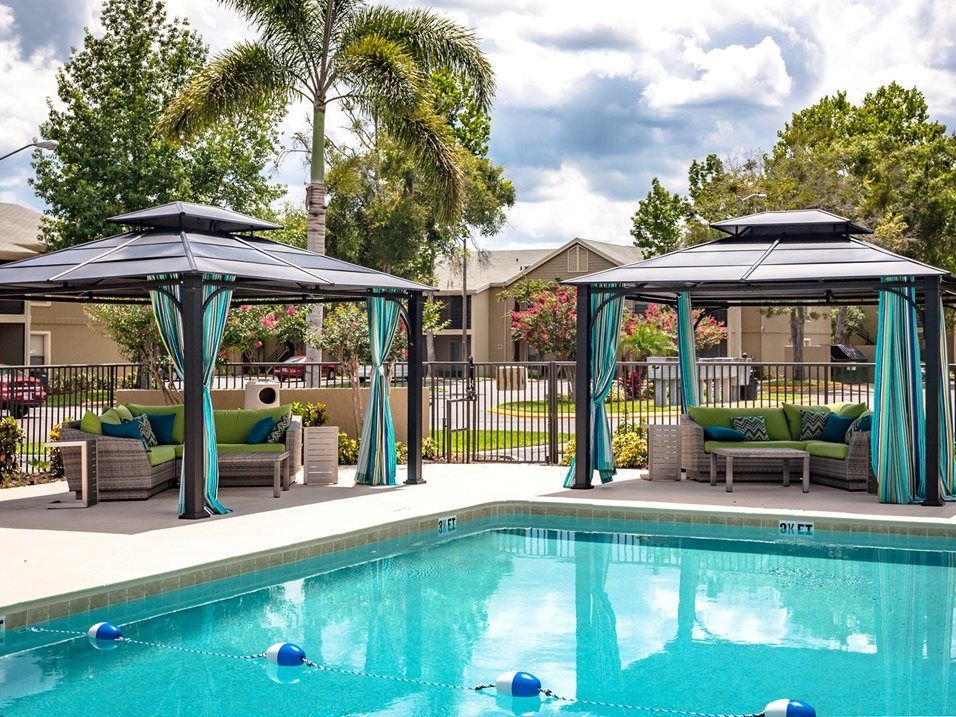 Swimming pool with two shaded lounge areas and blue curtains.