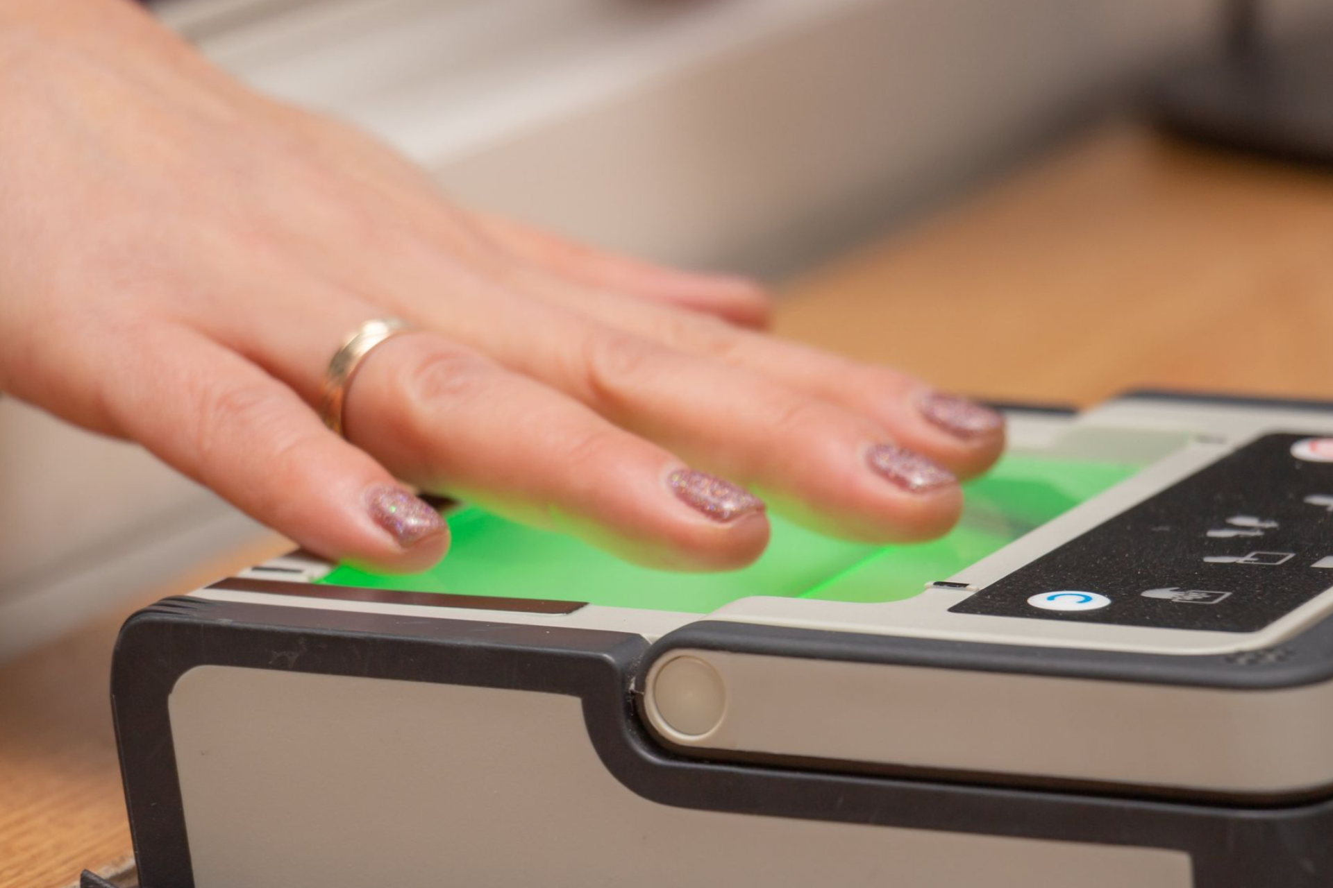 Hand with a ring on a fingerprint scanner, illuminated in green, indoors.