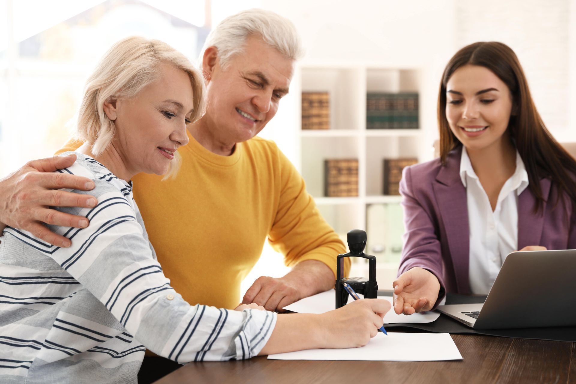 Senior couple signing papers with financial advisor in a bright office.