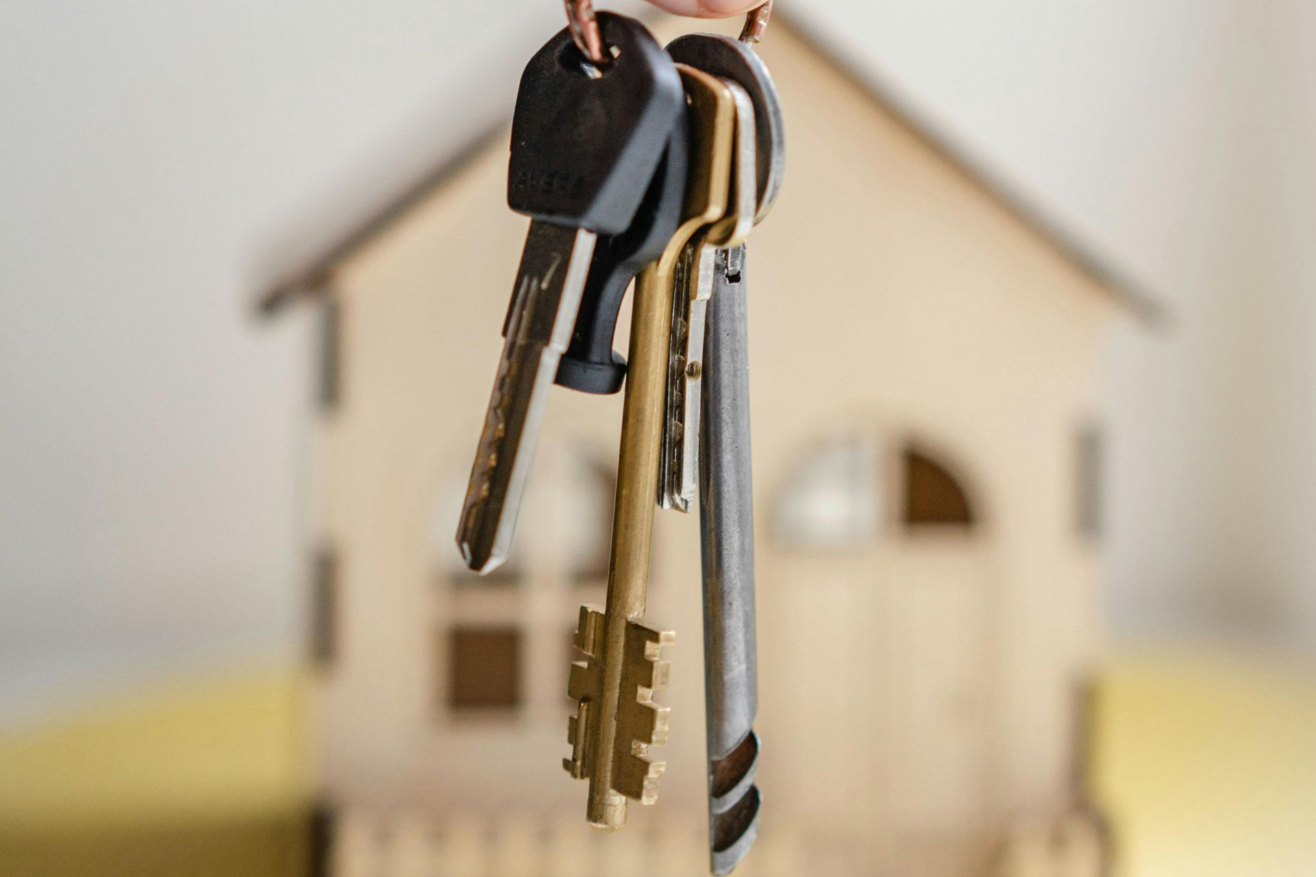 Keys in front of a blurred wooden house model, symbolizing homeownership.