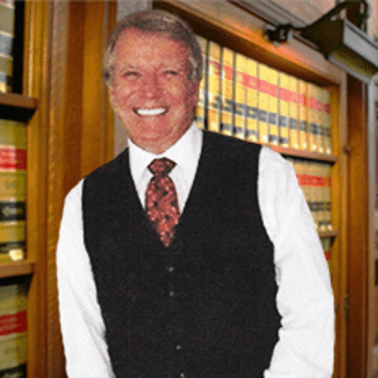 Smiling David Frost in a black vest and red tie standing in front of law books