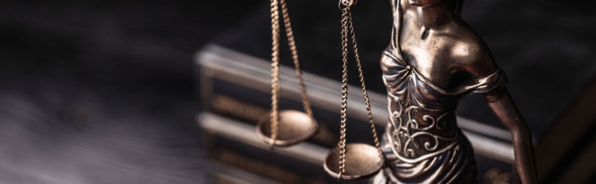 Bronze Lady Justice statue with scales on a law book, in warm dramatic lighting
