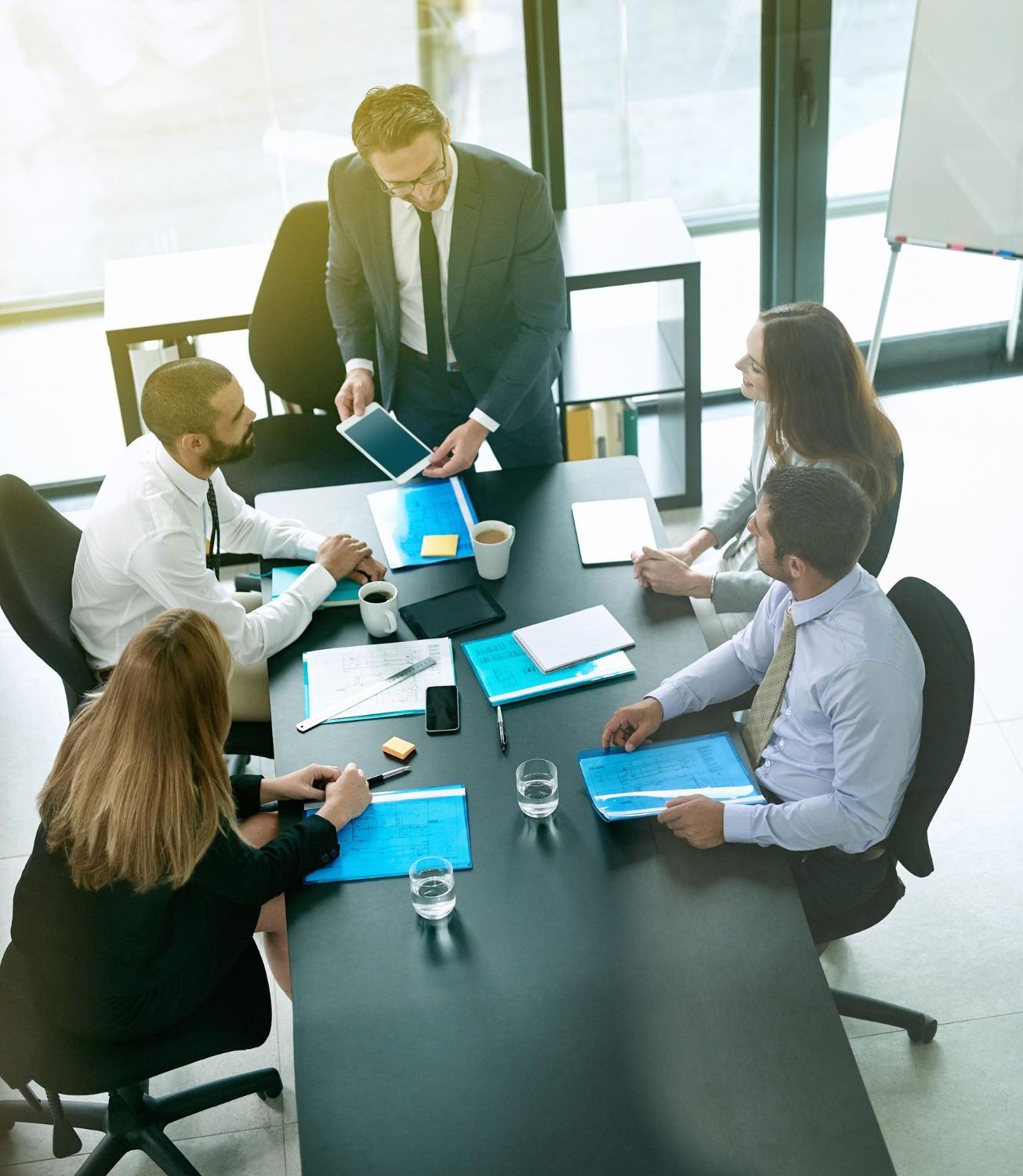 Team meeting in a bright office, with five people around a conference table reviewing documents and a laptop.