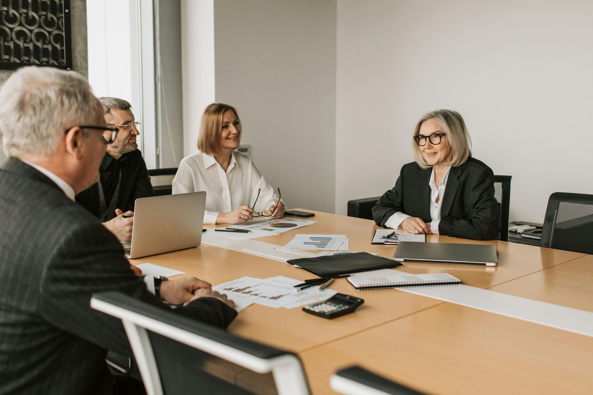 Business meeting around a conference table with four people, laptops, papers, and calculators in a bright office